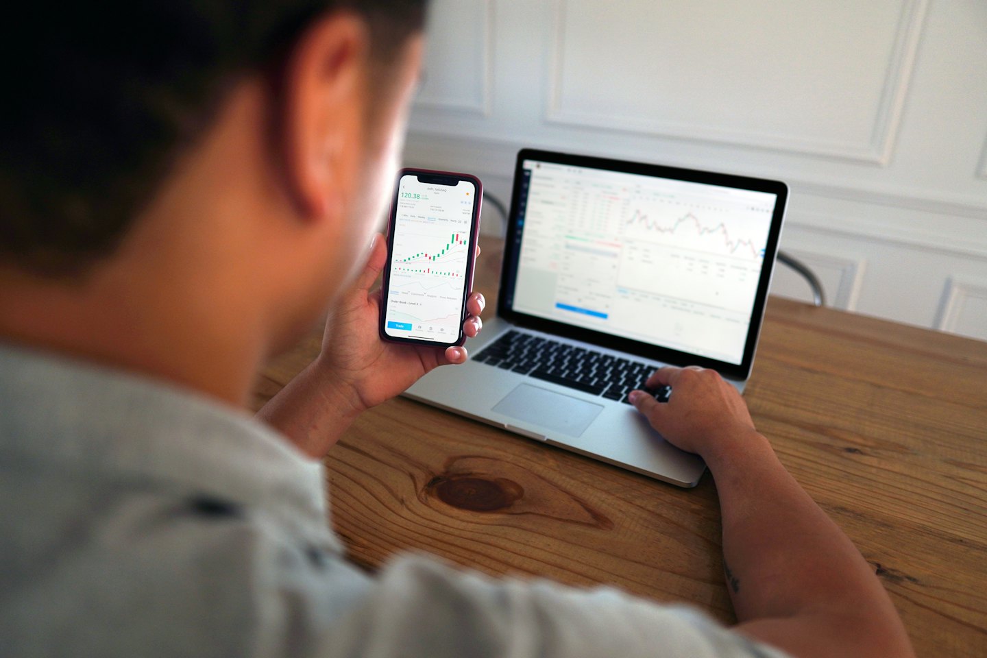 Person reviews stock charts on phone and laptop.