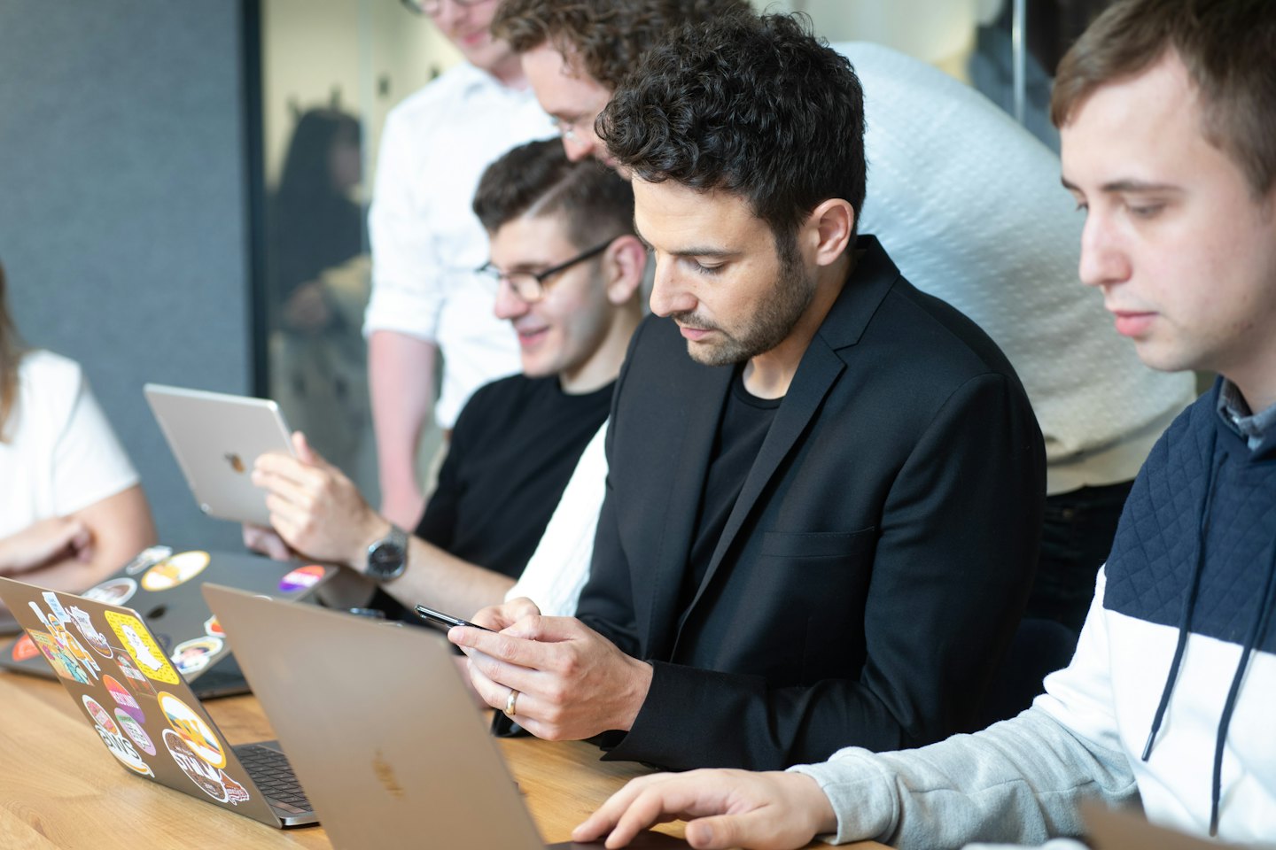 Professionals collaborating on laptops and smartphones at a wooden table.